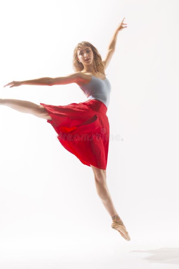 Young woman ballet dancer in pointe shoes and light blue leotard with a red skirt, dancing in the studio against a white background. Young woman ballet dancer in pointe shoes and light blue leotard with a red skirt, dancing in the studio against a white background