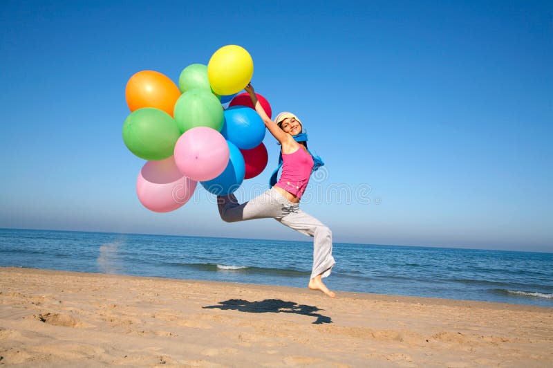 Young woman with balloons jumping on the beach