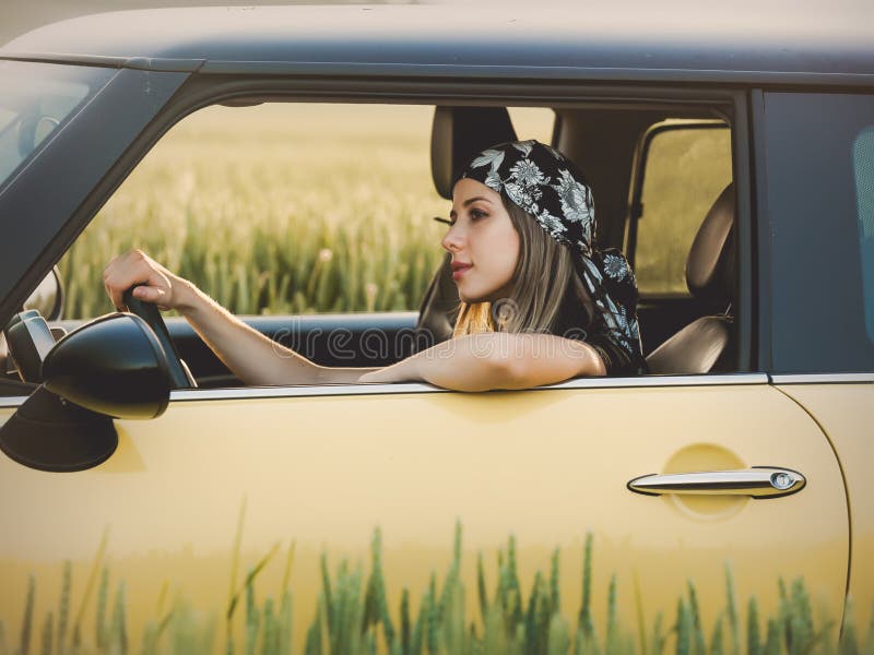 Young woman in a bandana drives a car on a rural road. Young woman in a bandana drives a car on a rural road