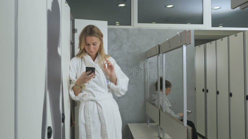 Young woman in bathrobe uses smartphone in dressing room