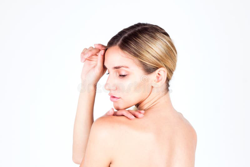Young woman with beautiful skin and a naked back looking down and touching her forehead.
