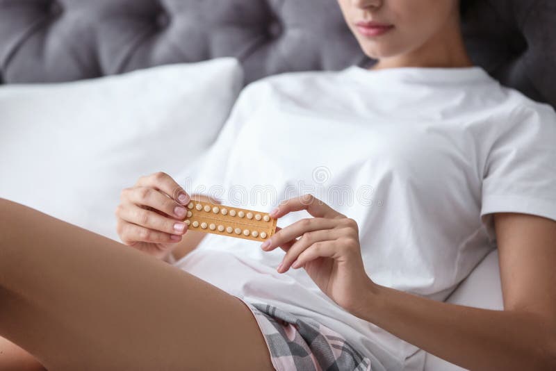 Young woman with birth control pills in bedroom