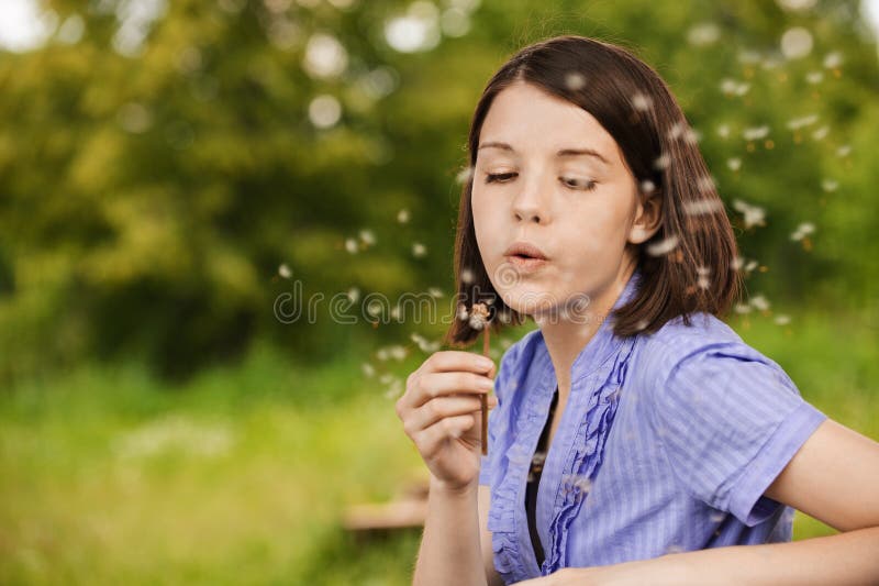 Young woman blowing on dandelion