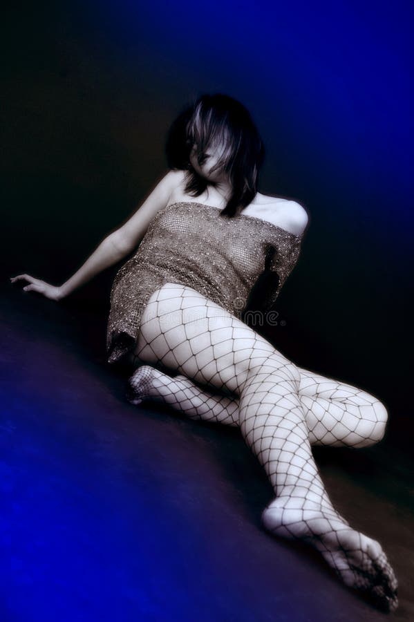 Angled portrait of a young woman stretched out on the floor, wearing an off-the-shoulder minidress and fishnet stockings. Her head is turned to her right so that her hair is falling over her face, mostly obscuring it. The model is desaturated except for her hair, which has a blue coloring to it. Shot from a viewpoint near the model's outstretched foot. Isolated on a black and blue background. Angled portrait of a young woman stretched out on the floor, wearing an off-the-shoulder minidress and fishnet stockings. Her head is turned to her right so that her hair is falling over her face, mostly obscuring it. The model is desaturated except for her hair, which has a blue coloring to it. Shot from a viewpoint near the model's outstretched foot. Isolated on a black and blue background.