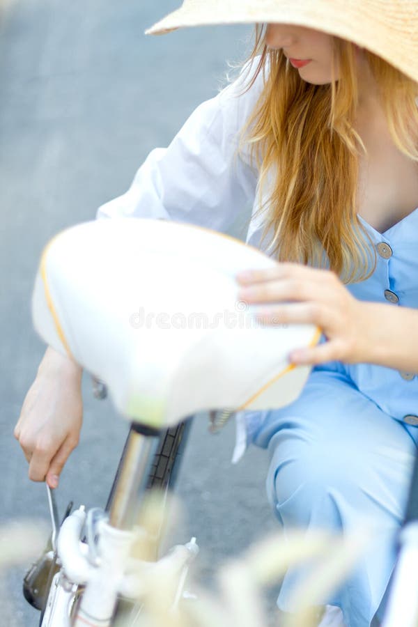 Woman in blue dress and straw hat is repairing white female bicycle royalty free stock photos Woman in blue dress and straw hat is repairing white female bicycle royalty free stock photos