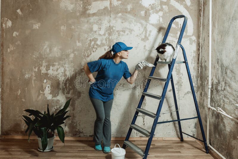 A young woman in a blue t-shirt and a baseball cap makes repairs in the apartment.