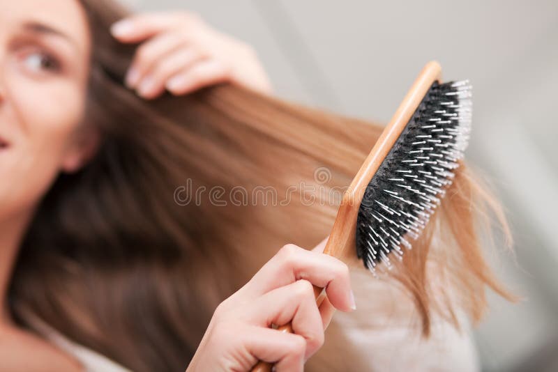 Young woman in pyjama brushing her long dark-blond hair after getting up in the morning; focus on brush!. Young woman in pyjama brushing her long dark-blond hair after getting up in the morning; focus on brush!