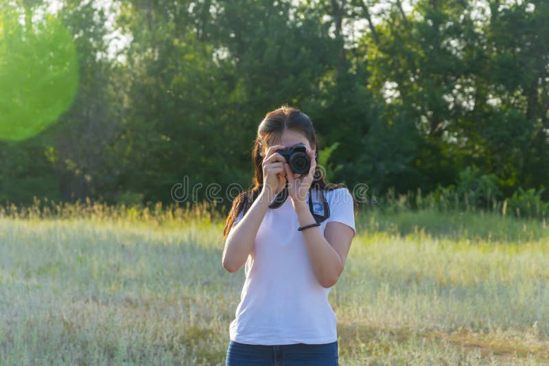 Young woman with camera lens. A beautiful brunette photographer is taking pictures in nature on a summer day