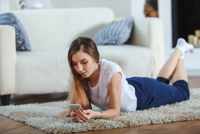 Young woman checking her smart phone lying on carpet stock photography Young woman checking her smart phone lying on carpet stock photography