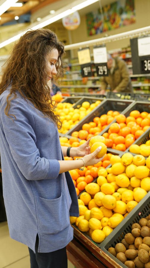 Young woman chooses fruits in grocer`s shop, touches to lemons, make purchases in supermarket, eats healthy food. People, stock images Young woman chooses fruits in grocer`s shop, touches to lemons, make purchases in supermarket, eats healthy food. People, stock images
