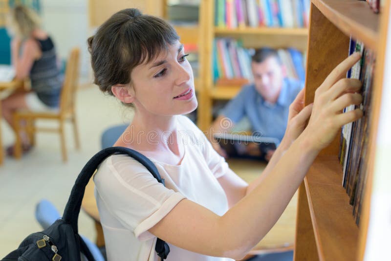 Young woman choosing book from library shelf royalty free stock photos