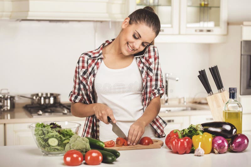 Young woman chopping vegetables and talking on phone.