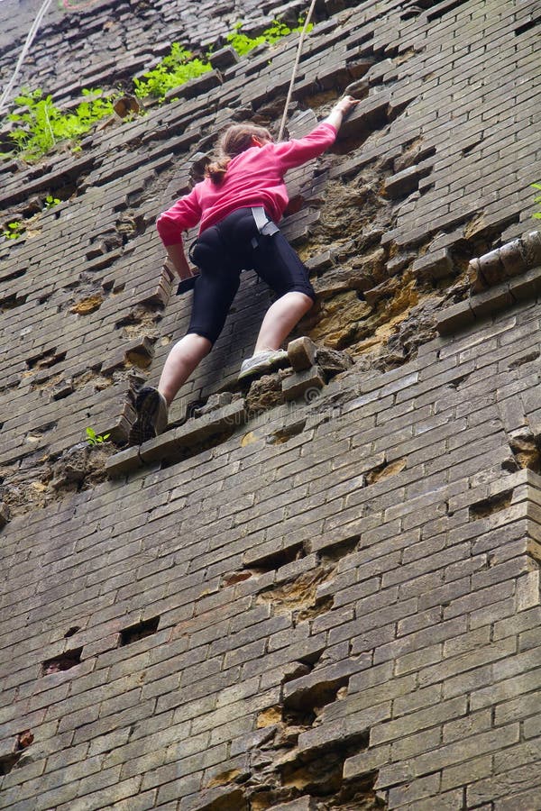 Young woman climbing up brick wall