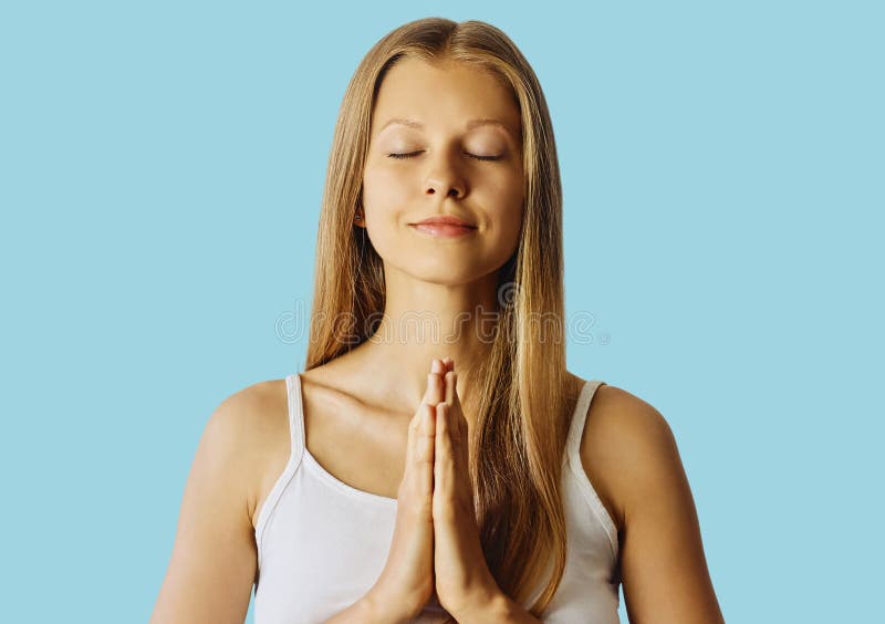 Young woman with closed eyes and hands in praying gesture. Meditation, balance and peace of mind concept. over blue royalty free stock photography Young woman with closed eyes and hands in praying gesture. Meditation, balance and peace of mind concept. over blue royalty free stock photography