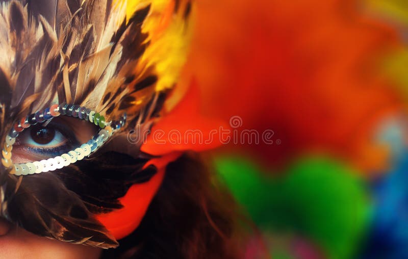 Young woman with a colorful feather carnival face mask on bright colorful background, eye contact, make up artist.