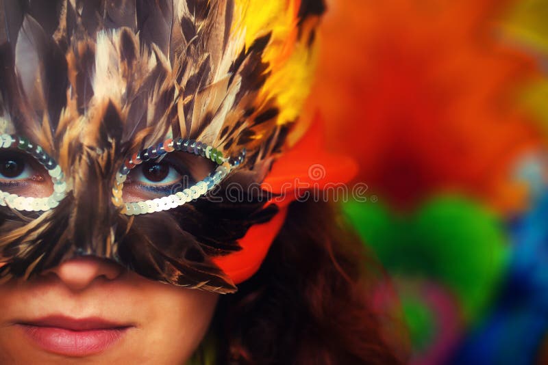 Young woman with a colorful feather carnival face mask on bright colorful background, eye contact, make up artist.