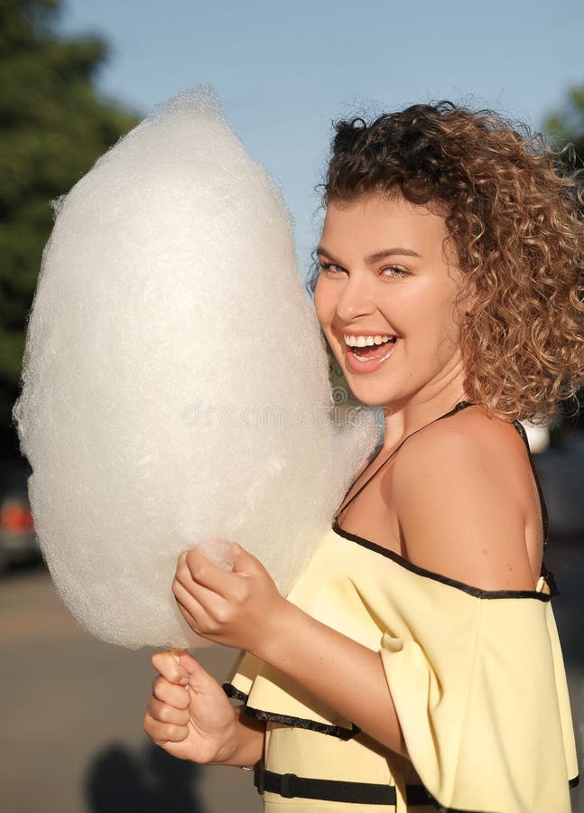 Smiling woman with curly hair has fun with cotton candy at sunset