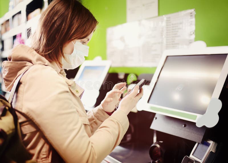 Young woman customer wearing disposable medical face mask make payment with smartphone contactless method in supermarket. Paypass royalty free stock photography Young woman customer wearing disposable medical face mask make payment with smartphone contactless method in supermarket. Paypass royalty free stock photography