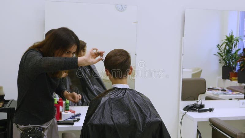 Young woman cutting hair at the hairdresser. Hairstylist cuts the hair to a young girl with a professional scissors