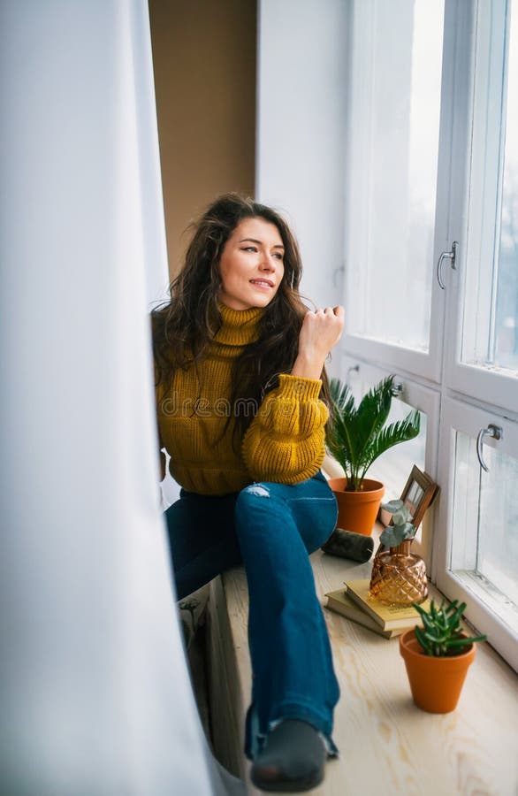 Young woman daydreaming on a beautiful day, sits by a window on sill stock photo Young woman daydreaming on a beautiful day, sits by a window on sill stock photo