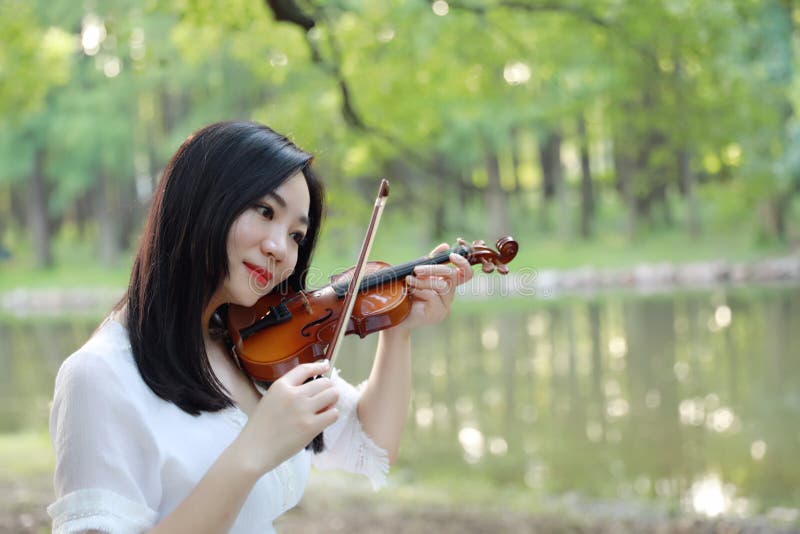 Young woman Dedicated playing violin ,Silhouette of teenage violin player over sunset on river,lake