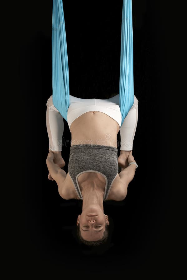Young woman demonstrates inverted asanas during fly yoga. Girl practices anti-gravity yoga upside down. Black background royalty free stock photography
