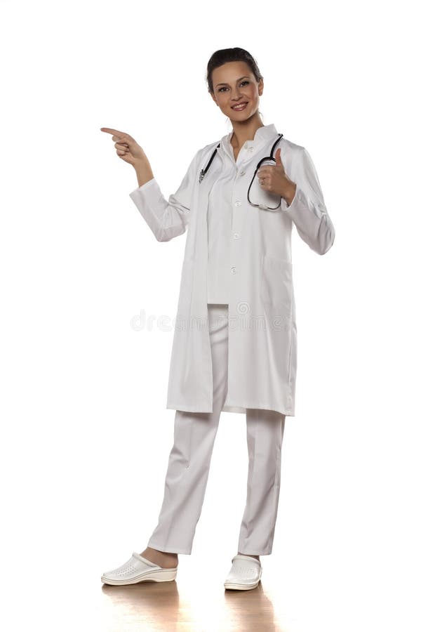 Young woman doctor in a uniform pointing at empty space and showing thumb up