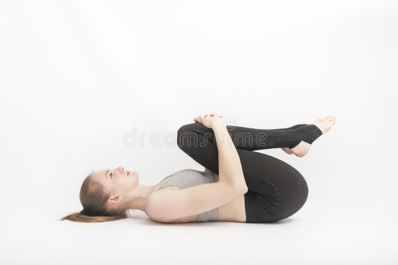 Young woman does yoga with her knees to her chest on white background. Technique of performing asanas. meditation