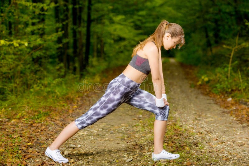 Young woman doing stretching exercise on road forest