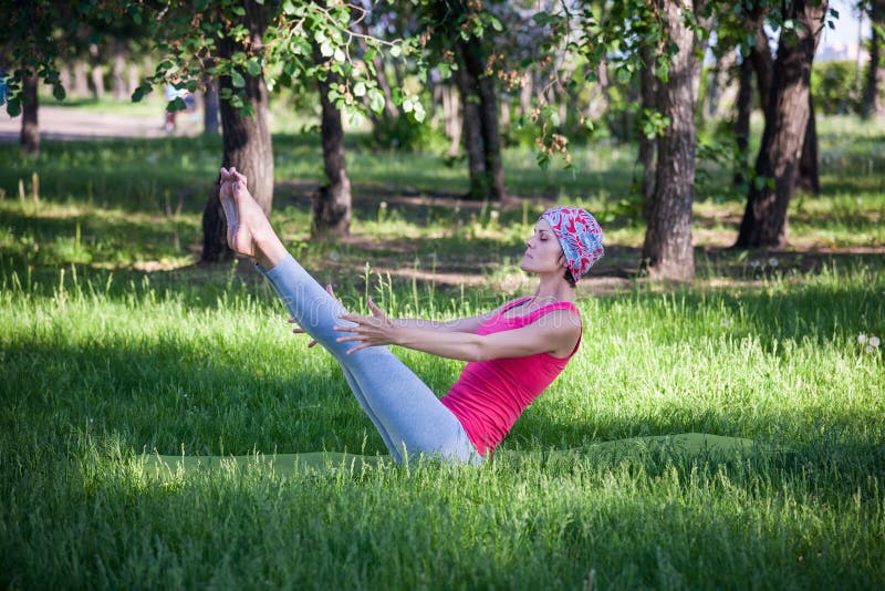 Young woman doing yoga and gymnastics in the park. boat pose