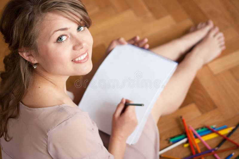 Pretty young woman drawing for fun while sitting on the floor