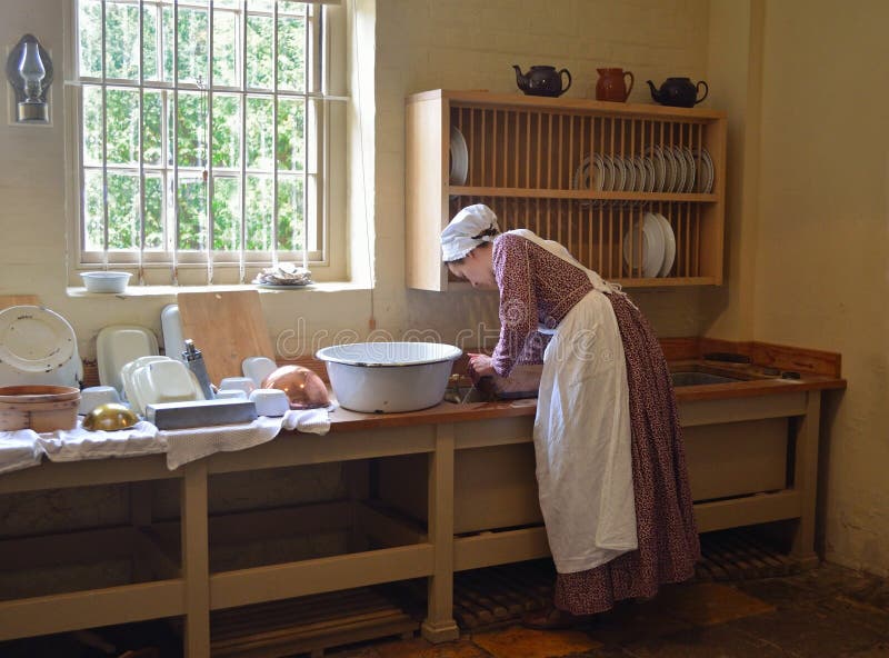 Young woman dressed as Victoria kitchen maid washing dishes in sink