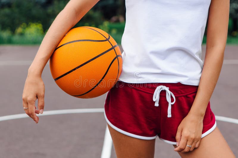 Young woman dressed in white t-shirt, shorts holding a ball on a basketball court. stock images Young woman dressed in white t-shirt, shorts holding a ball on a basketball court. stock images