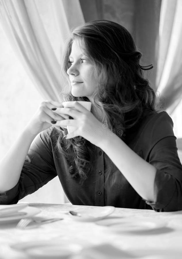 Young woman drinking coffee in a cafe. Black and white photo. royalty free stock photography