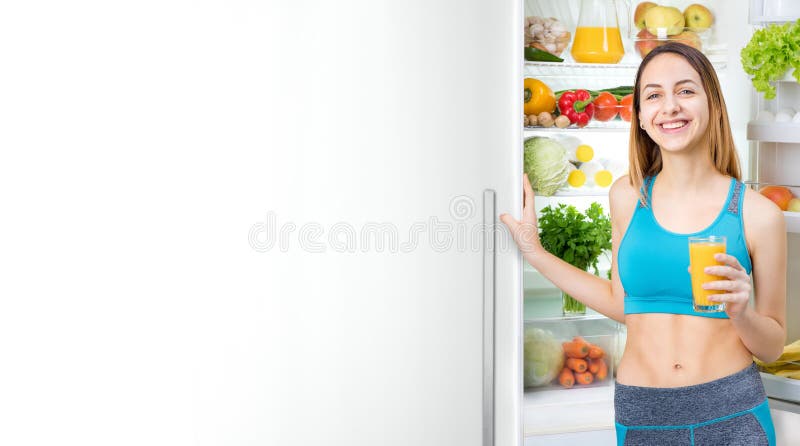 Young woman drinking juice and staying near the fridge full of health food. stock image Young woman drinking juice and staying near the fridge full of health food. stock image