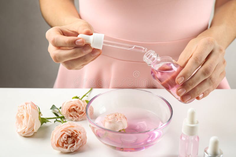 Young woman dripping rose essential oil into glass bottle at table
