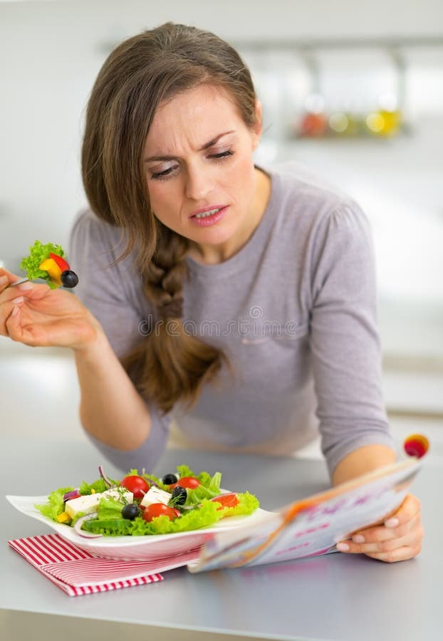 Young woman eating greek salad in kitchen and read stock images Young woman eating greek salad in kitchen and read stock images