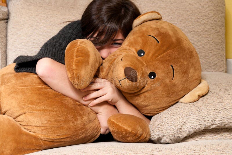 Young woman embracing teddy bear lying on on sofa