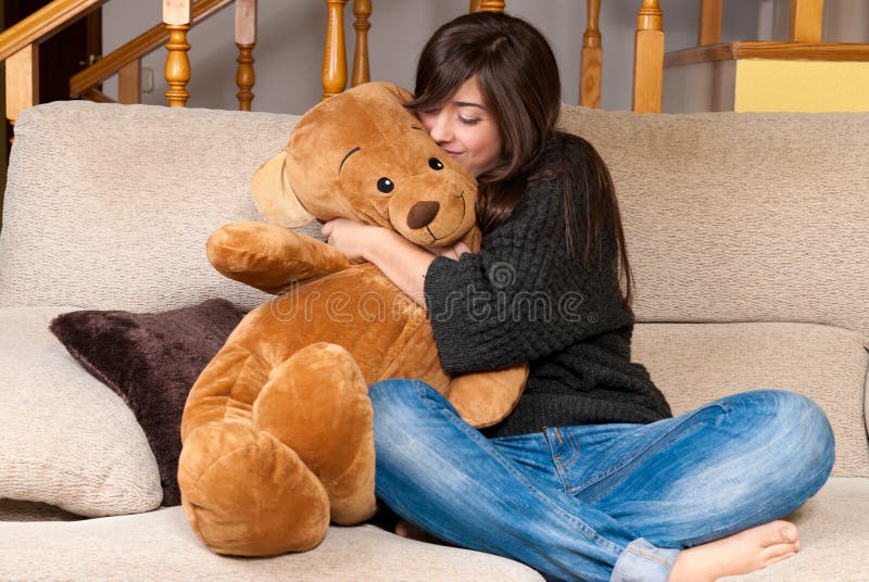 Young woman embracing teddy bear sitting on sofa