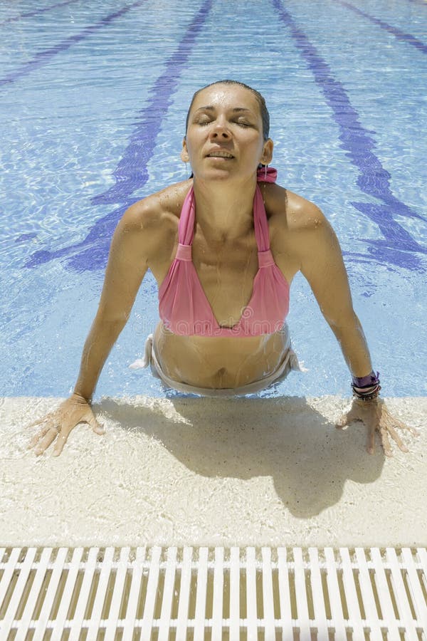 Young woman emerging from the water in the swimming pool edge with her eyes...