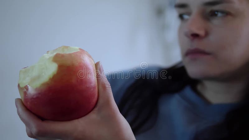 Young woman enjoys the fresh taste of an apple chewing contentedly. Apple in hand, her enjoyment is evident. Each bite