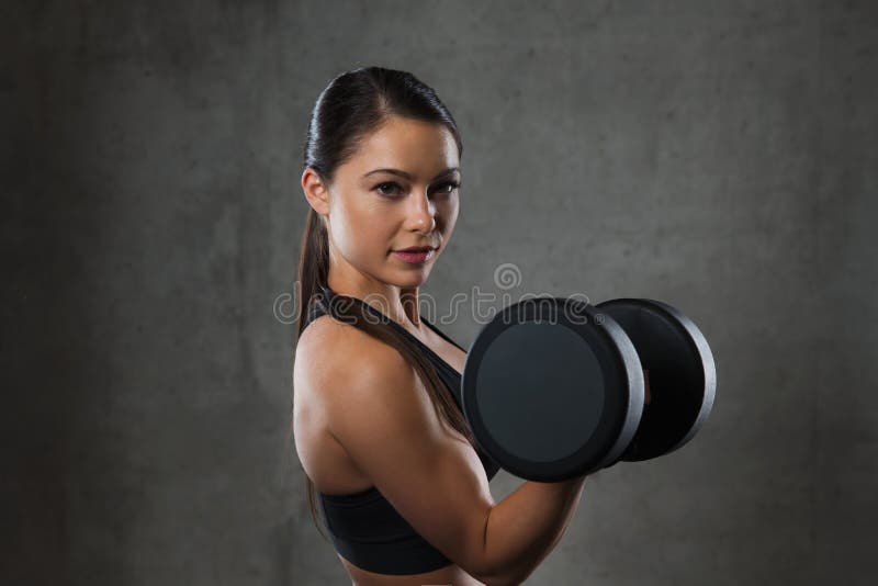 Fitness, sport, exercising, training and people concept - young woman flexing muscles with dumbbells in gym