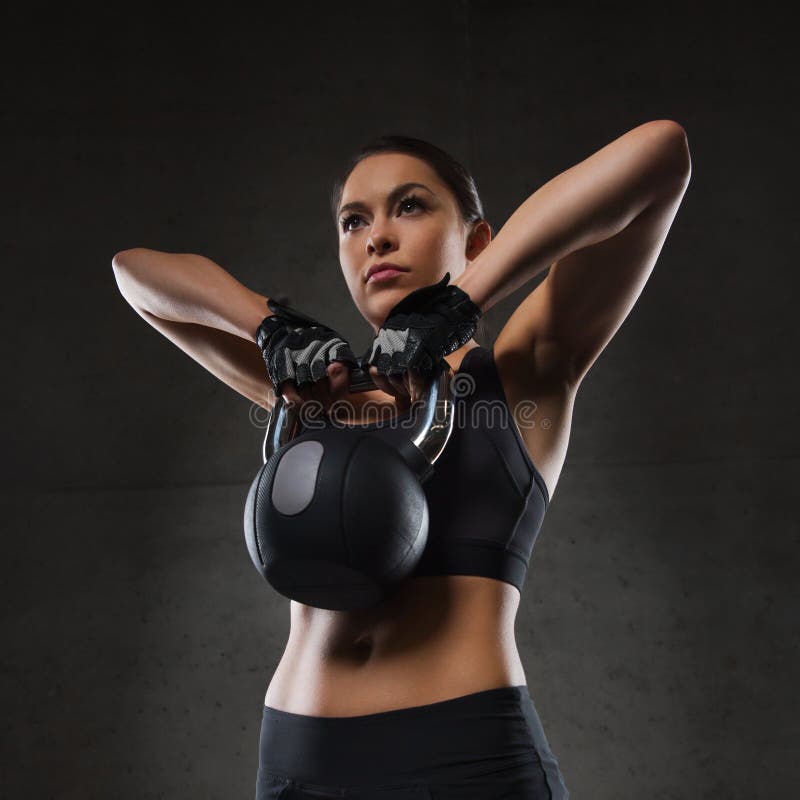 Fitness, sport, exercising, weightlifting and people concept - young woman flexing muscles with kettlebell in gym