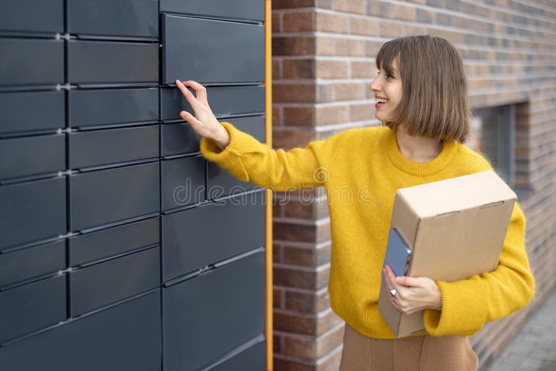 Woman getting parcel from cell of automatic post terminal outdoors. Young woman getting parcel from cell of automatic post terminal outdoors. Concept of
