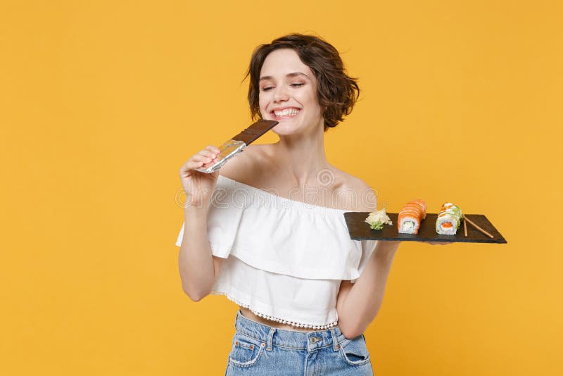 Young woman girl hold in hand choice between chocolate bar makizushi sushi roll served on black plate traditional stock photo