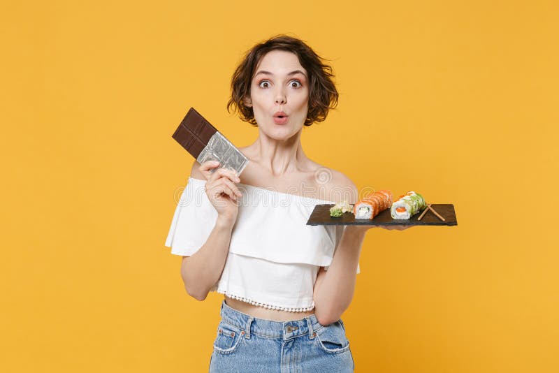 Young woman girl hold in hand choice between chocolate bar makizushi sushi roll served on black plate traditional stock photo