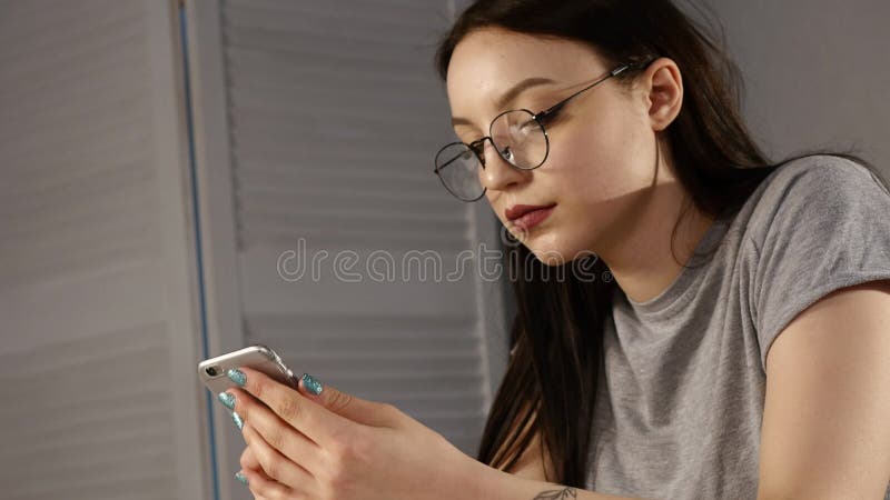 Young woman with glasses browsing photos on smartphone. reflected in the glasses