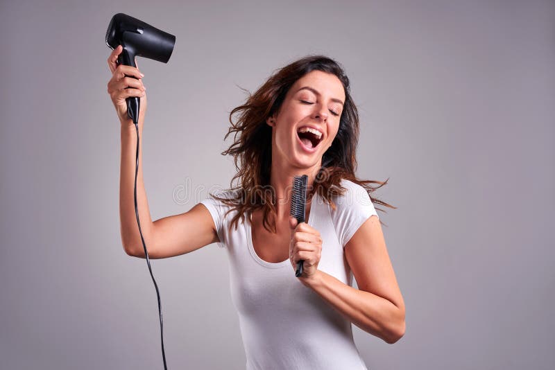 A beautiful young woman feeling happy and singing while using a hairdryer and a hairbrush.r. A beautiful young woman feeling happy and singing while using a hairdryer and a hairbrush.r