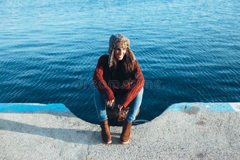 Young woman in hat and casual clothes sitting on pier stock photo Young woman in hat and casual clothes sitting on pier stock photo