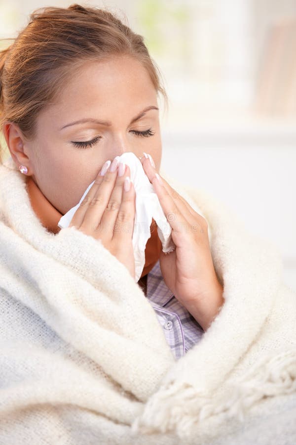 Young woman having flu blowing her nose